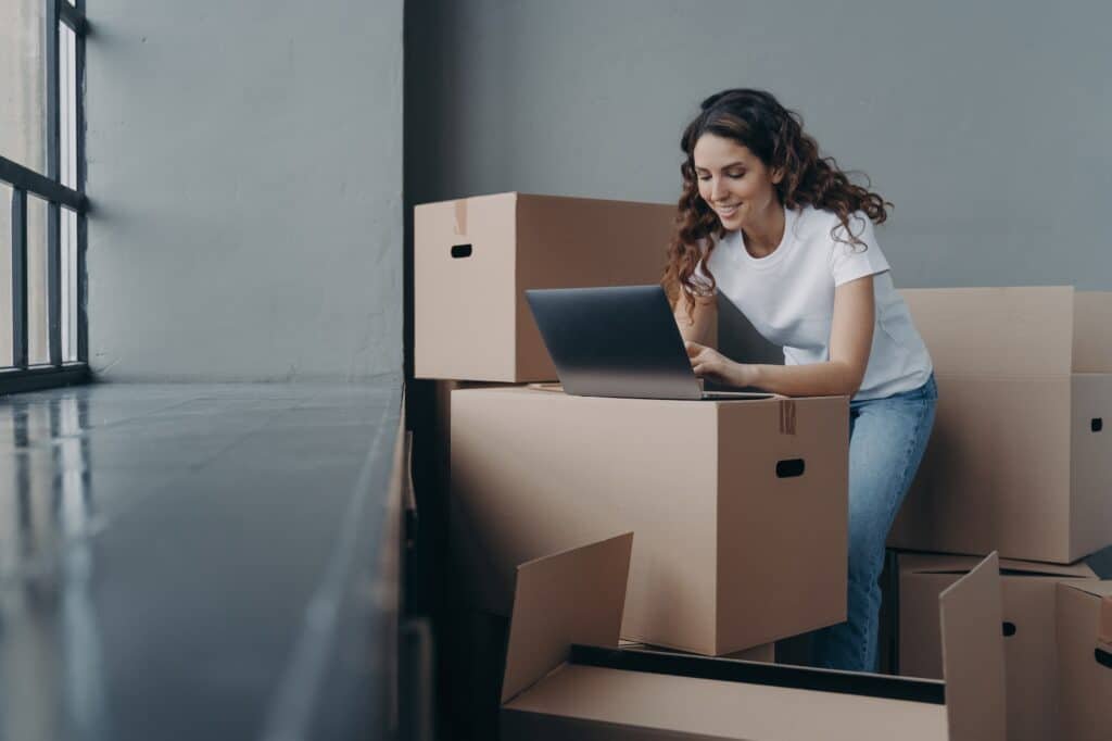 Female with boxes works at laptop orders moving company shopping online Ecommerce relocation day