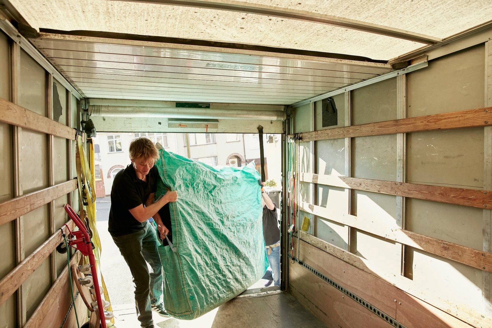 Removals business A man lifting an item of furniture covered in green plastic into a removals van